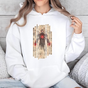 May include: White hoodie featuring a graphic of Iron Man. The design shows Iron Man's armor with a red chest piece, set against a backdrop of vertical, aged paper strips. The hoodie has a drawstring hood and a kangaroo pocket.