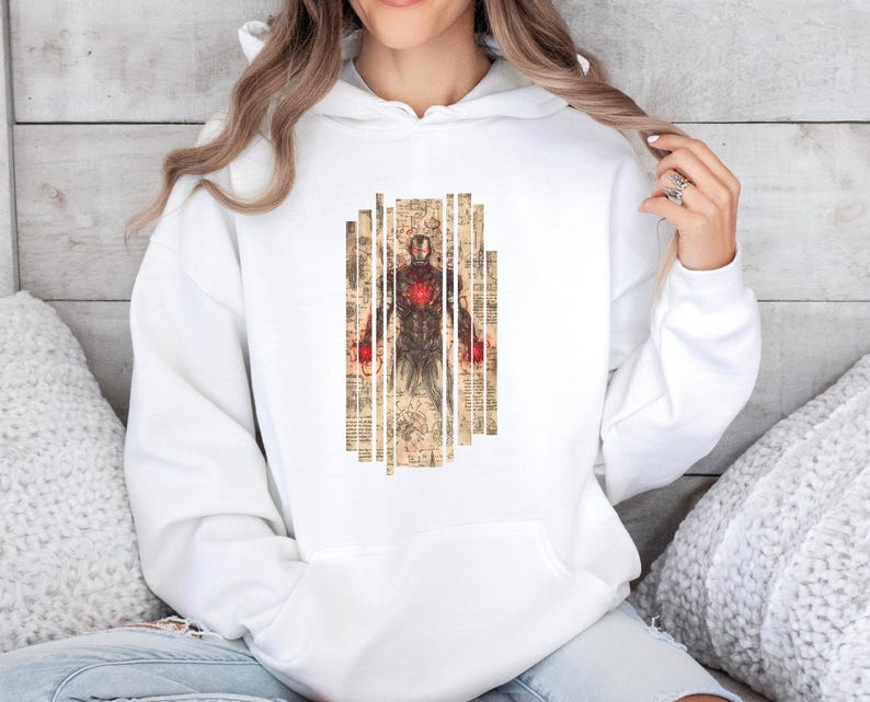 May include: White hoodie featuring a graphic of Iron Man. The design shows Iron Man's armor with a red chest piece, set against a backdrop of vertical, aged paper strips. The hoodie has a drawstring hood and a kangaroo pocket.