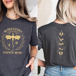 Pode incluir: Duas camisetas cinzas com um gr&aacute;fico de drag&atilde;o e o texto "Wingleader Riders Quadrant Fourth Wing". Uma camiseta tem uma fileira vertical de silhuetas de drag&otilde;es.