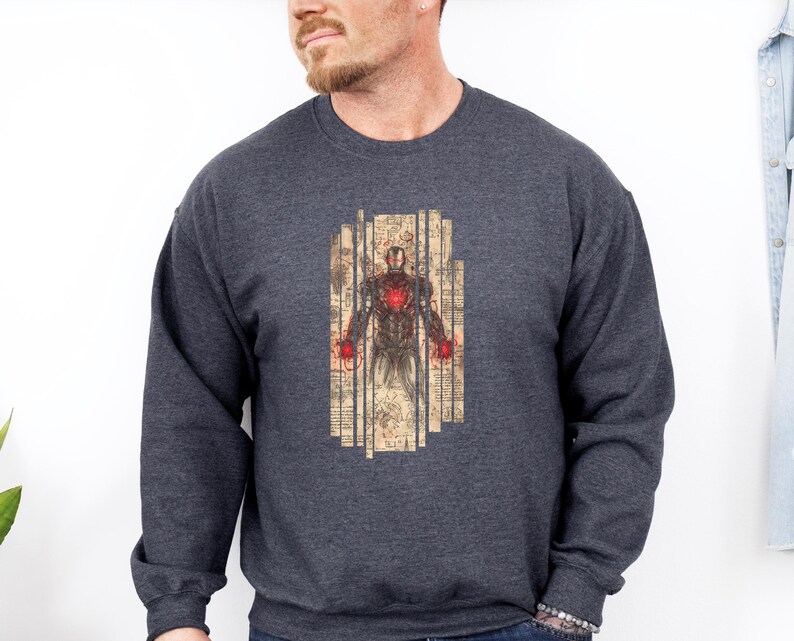 May include: A dark gray sweatshirt featuring a detailed illustration of Iron Man. The graphic is in a vertical rectangular shape with a vintage, aged paper look. The Iron Man design has red and gold accents.