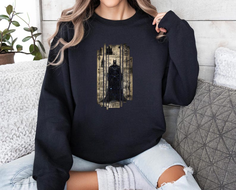 Puede incluir: Sudadera negra con un gr&aacute;fico de Batman. El gr&aacute;fico muestra a Batman dentro de un marco vertical, sobre un fondo de papel vintage. La sudadera es de color negro liso y tiene mangas largas.