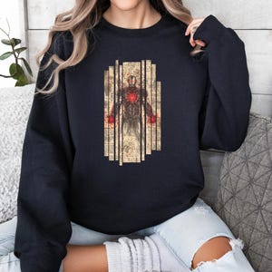 May include: A black sweatshirt featuring a graphic of a figure with a red heart and red hands, set against a backdrop of vertical beige panels with vintage-style text. The design is centered on the front of the sweatshirt.