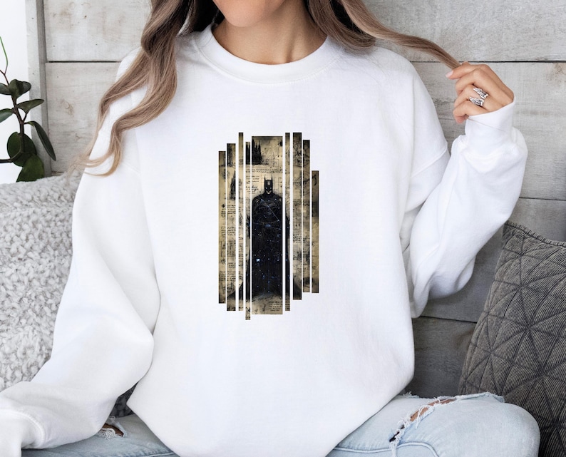Puede incluir: Sudadera blanca con un gr&aacute;fico de Batman. El gr&aacute;fico es una silueta negra de Batman sobre un fondo de papel vintage y rayas verticales. Una prenda casual y c&oacute;moda.