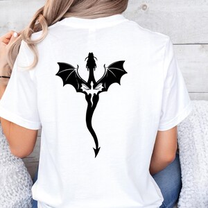 May include: White t-shirt with a black silhouette of a dragon with wings spread out on the back.