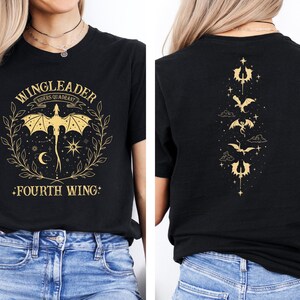 Pode incluir: Camiseta preta com texto e gr&aacute;fico dourados. A frente da camiseta diz "Wingleader Riders Quadrant Fourth Wing". As costas da camiseta t&ecirc;m um desenho vertical de cinco drag&otilde;es com estrelas e nuvens.