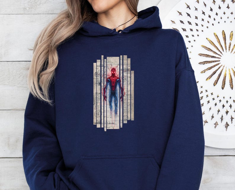 K&ouml;nnte beinhalten: Marineblauer Kapuzenpullover mit einer Grafik eines Superhelden in einem rot-blauen Anzug. Der Superheld ist in einer stilisierten, k&uuml;nstlerischen Weise dargestellt, vor dem Hintergrund vertikaler, gealterter papierartiger Tafeln. Der Hoodie hat eine Vordertasche und eine Kapuze mit Kordelzug.