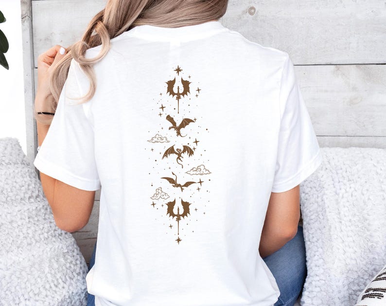 Pode incluir: Camiseta branca com um gr&aacute;fico marrom de um drag&atilde;o voando atrav&eacute;s de nuvens e estrelas.