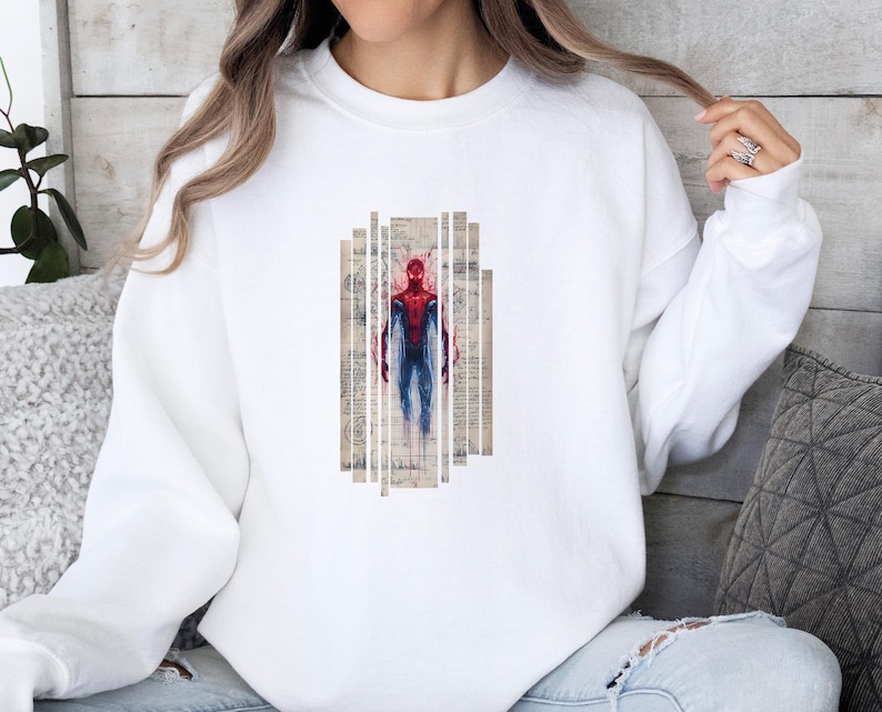 Op de afbeelding: Witte sweatshirt met een Spiderman-afbeelding. De afbeelding toont Spiderman in rood en blauw, tegen een achtergrond van vintage papieren stroken. De sweatshirt is effen wit van kleur.