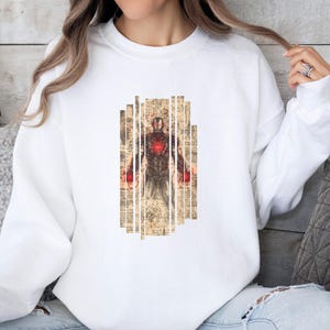 May include: White sweatshirt featuring a graphic of Iron Man in a vintage style. The design includes a detailed illustration of the character with red and brown tones, set against a background of aged paper.