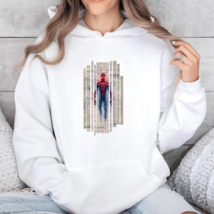 K&ouml;nnte beinhalten: Wei&szlig;er Kapuzenpullover mit einem Spiderman-Motiv. Das Motiv zeigt Spiderman in einem rot-blauen Anzug vor einem Hintergrund im Vintage-Stil. Der Kapuzenpullover ist aus weichem Material und hat ein klassisches Design.