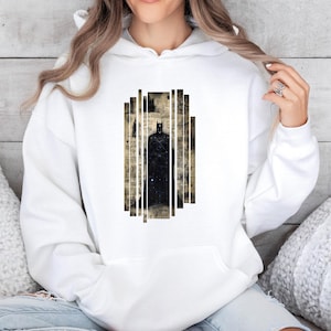 May include: White hoodie featuring a black Batman graphic. The graphic is a stylized image of Batman within a rectangular design. The design has a vintage newspaper background. The hoodie has a drawstring hood and a kangaroo pocket.