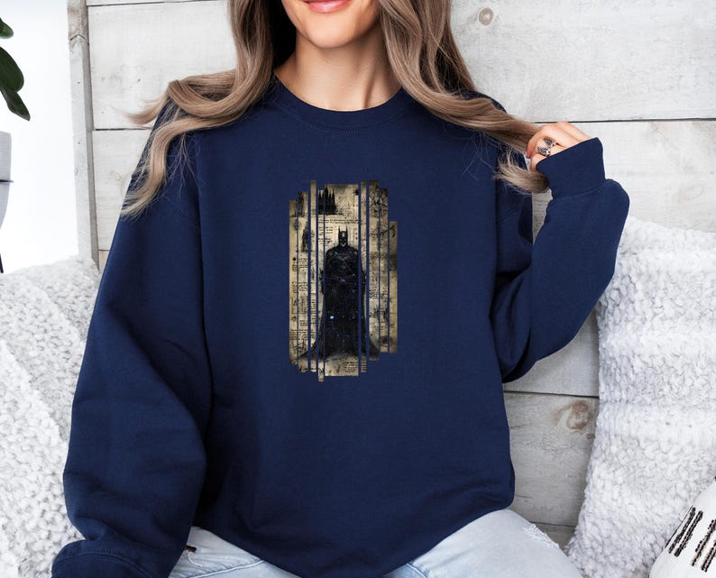 Puede incluir: Sudadera azul marino con un gr&aacute;fico de Batman. El gr&aacute;fico representa a Batman frente a un fondo de notas musicales y un paisaje urbano. La sudadera tiene mangas largas y cuello redondo.