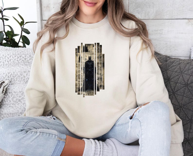 Puede incluir: Sudadera beige con un gr&aacute;fico de Batman. El dise&ntilde;o muestra una silueta negra de Batman dentro de un marco rectangular con un fondo de estilo peri&oacute;dico vintage. La sudadera es de color neutro.