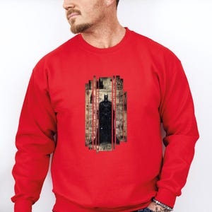 Puede incluir: Una sudadera roja con un gr&aacute;fico de Batman. El gr&aacute;fico muestra a Batman frente a un paisaje urbano con l&iacute;neas verticales rojas. El dise&ntilde;o est&aacute; impreso sobre un fondo de estilo vintage.