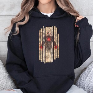 May include: Black hooded sweatshirt featuring a graphic of Iron Man in a vintage style. The design includes a detailed illustration of the character with a red glowing chest and hands, set against a backdrop of vertical lines.