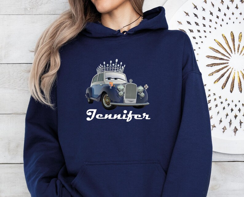 Puede incluir: Sudadera con capucha azul marino con un coche de dibujos animados con una corona. El coche es azul y plateado con un dise&ntilde;o vintage. El nombre "Jennifer" est&aacute; escrito en blanco debajo. La sudadera tiene un bolsillo delantero y una capucha con cord&oacute;n.