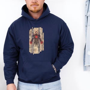 May include: Navy blue hooded sweatshirt featuring a graphic of a superhero. The graphic is a detailed illustration of a figure with a red chest and red hands, set against a backdrop of vertical lines. The sweatshirt has a front pocket.