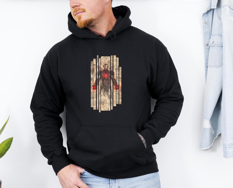 May include: Black hooded sweatshirt featuring a graphic of a figure with a red heart and red accents. The graphic is framed by vertical beige lines. The sweatshirt has a front pocket and a hood.