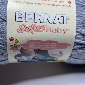 May include: A skein of Bernat Softee Baby yarn in a light blue color. The label reads "100% Acrylic, 140g/5oz, Sport D.K., Tricot léger, Jersey Ligero, Approx 331m/362yds", and "Free Pattern on Label, Patron gratuit au verso, Patrón gratuito en linea".