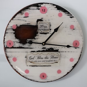 May include: A white and brown wooden clock with pink polka dots and the text "God Bless this Home - with love and laughter -" on the face. The clock has black hands and a gold center.