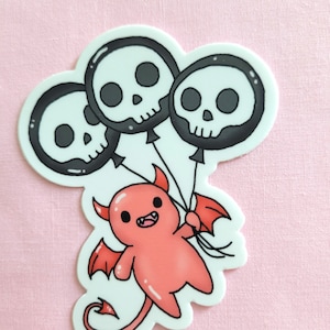 May include: A red cartoon devil with horns and wings holding three black skull-shaped balloons.