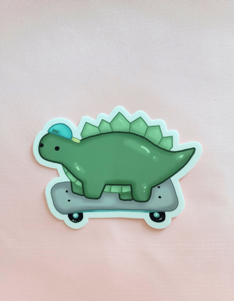 May include: A green dinosaur wearing a blue hat is riding a skateboard. The dinosaur has a spiky back and is facing to the right. The skateboard is grey with black wheels.