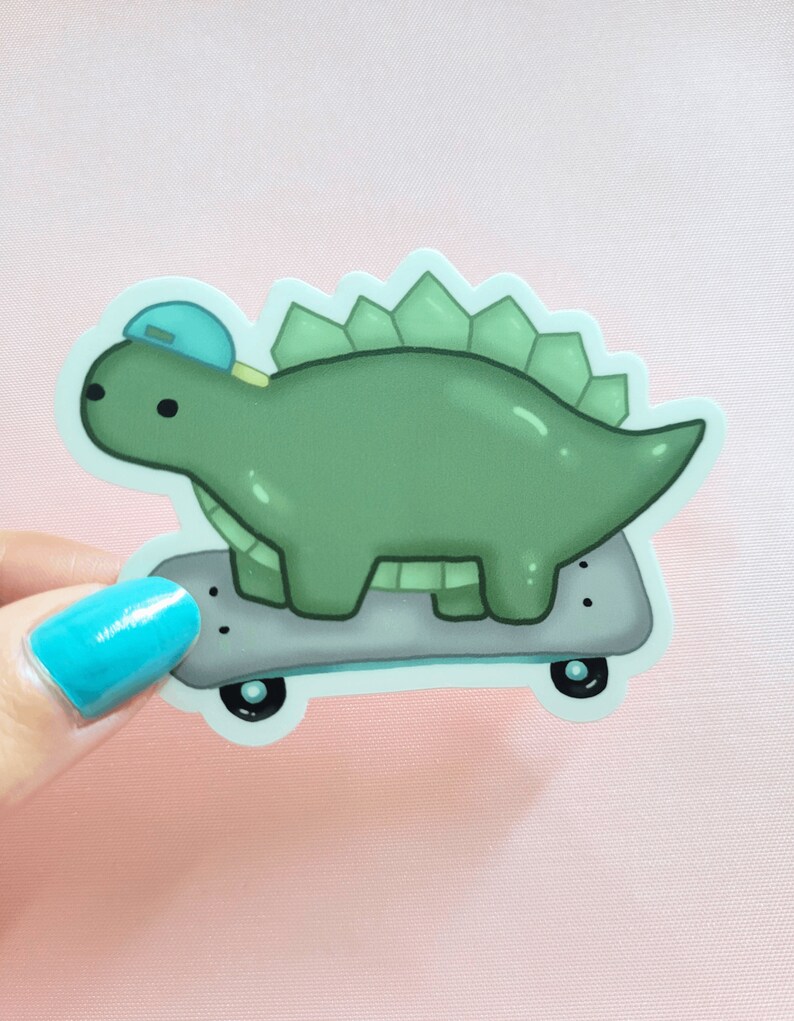 May include: A green dinosaur wearing a blue hat is skateboarding. The dinosaur has a spiky back and is on a grey skateboard with black wheels.