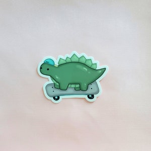May include: A green dinosaur wearing a blue hat is skateboarding. The dinosaur has a light green body and dark green spikes on its back. The skateboard is black with white wheels.