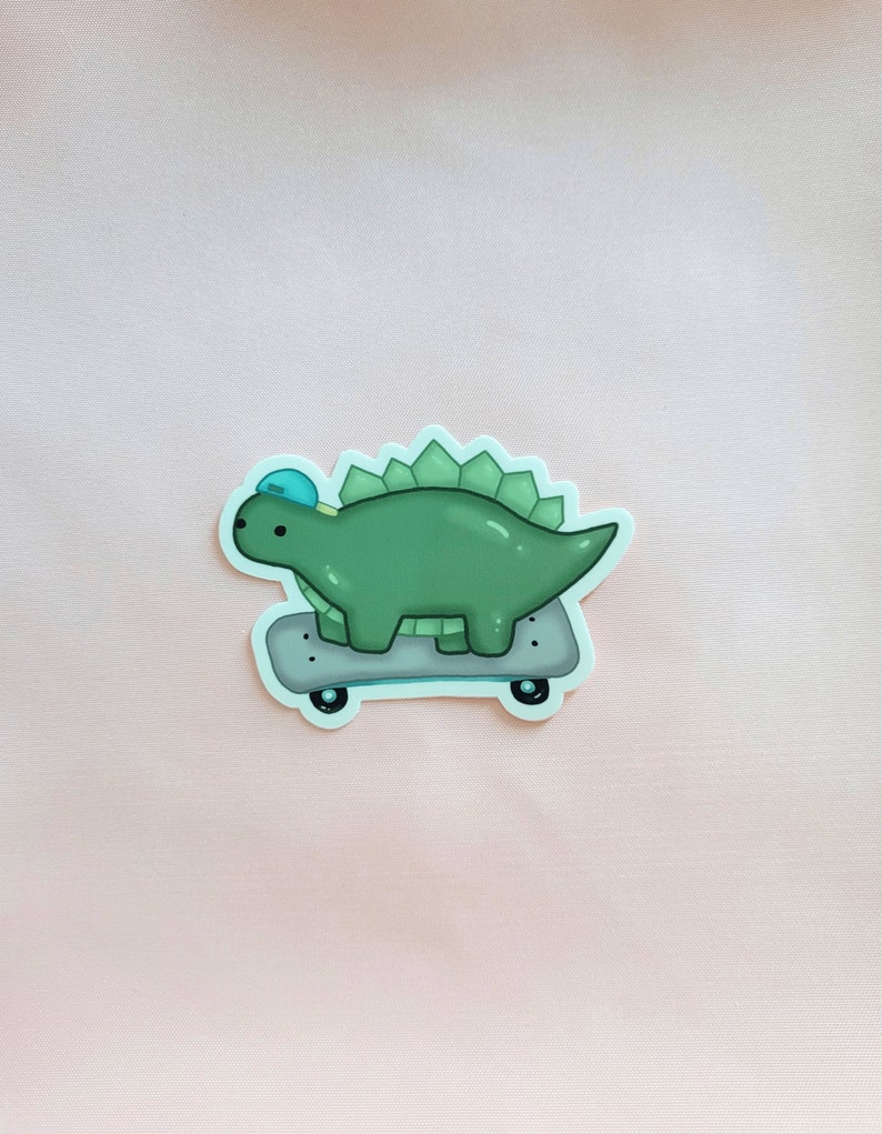 May include: A green dinosaur wearing a blue hat is skateboarding. The dinosaur has a light green body and dark green spikes on its back. The skateboard is black with white wheels.