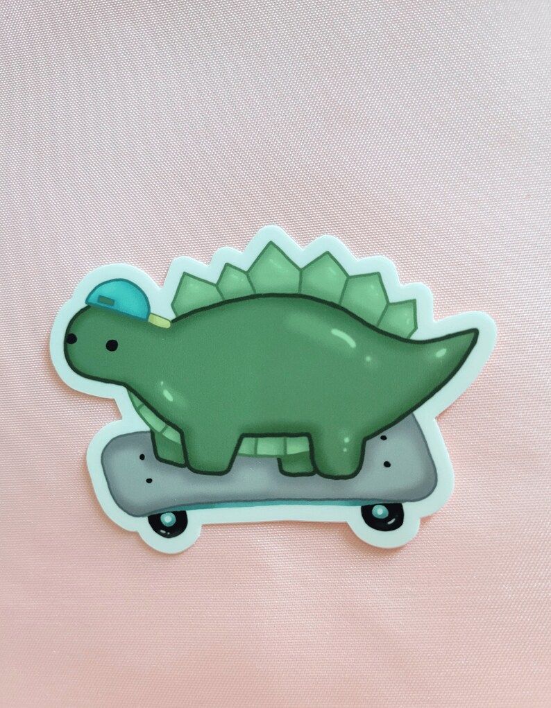 May include: A green dinosaur wearing a blue baseball cap is riding a skateboard with black wheels. The dinosaur has a spiky back and a long tail.
