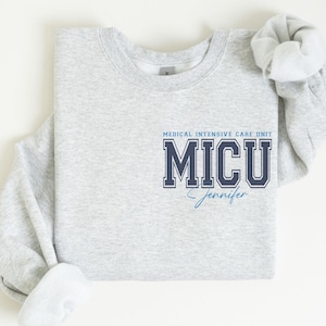 May include: A gray sweatshirt with the text "MEDICAL INTENSIVE CARE UNIT" and "MICU" in navy blue with a blue outline. The name "Jennifer" is written in blue script below the text.