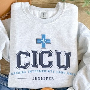 May include: Gray sweatshirt with a blue and white medical cross and the text "CICU Cardiac Intermediate Care Unit Jennifer".