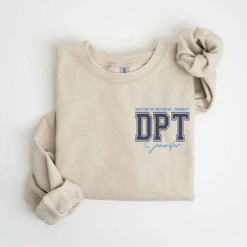 Puede incluir: Una sudadera beige con el texto "Doctor of Physical Therapy DPT Jennifer" impreso en la parte delantera.