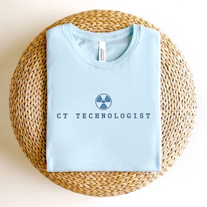 May include: Light blue t-shirt with a blue radiation symbol and the text "CT Technologist" printed on the front.