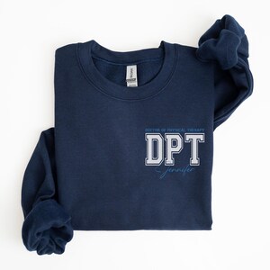 Puede incluir: Una sudadera azul marino con el texto "Doctor of Physical Therapy DPT Jennifer" impreso en la parte delantera.
