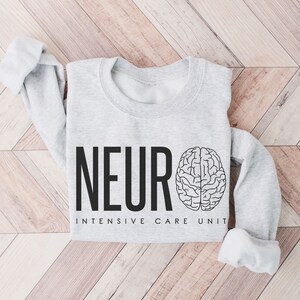 Puede incluir: Una sudadera gris con el texto "NEURO INTENSIVE CARE UNIT" y un gr&aacute;fico de cerebro.