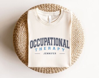May include: A beige t-shirt with the text "Occupational Therapy" in blue and black lettering. The name "Jennifer" is printed below the text.