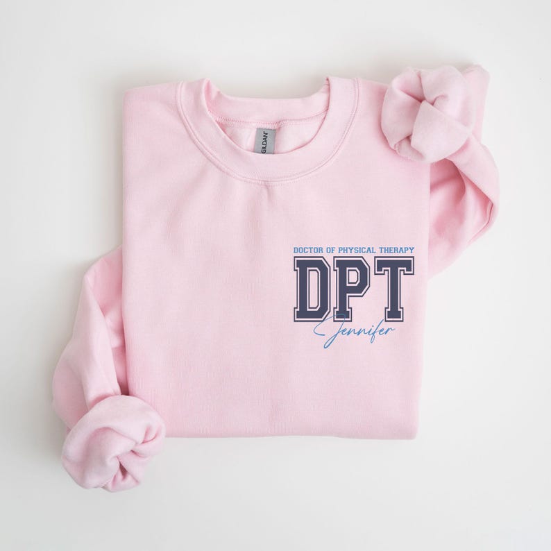 Puede incluir: Sudadera rosa con el texto "DOCTOR OF PHYSICAL THERAPY DPT Jennifer" en azul marino y azul claro.