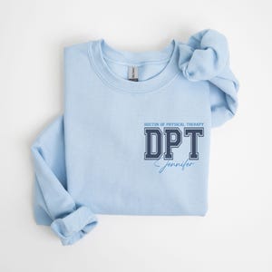 Puede incluir: Sudadera azul claro con un gr&aacute;fico azul marino que dice "DOCTOR OF PHYSICAL THERAPY DPT Jennifer".