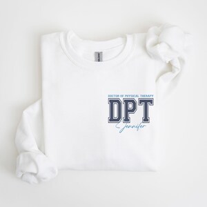 Puede incluir: Sudadera blanca con un gr&aacute;fico azul marino y blanco que dice "DOCTOR OF PHYSICAL THERAPY DPT Jennifer".
