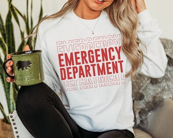 May include: White sweatshirt with the text "EMERGENCY DEPARTMENT" printed in red, stacked and repeated in a retro style. The sweatshirt is being worn by a person holding a green mug with a bear silhouette and the text "BEARY CHRISTMAS".