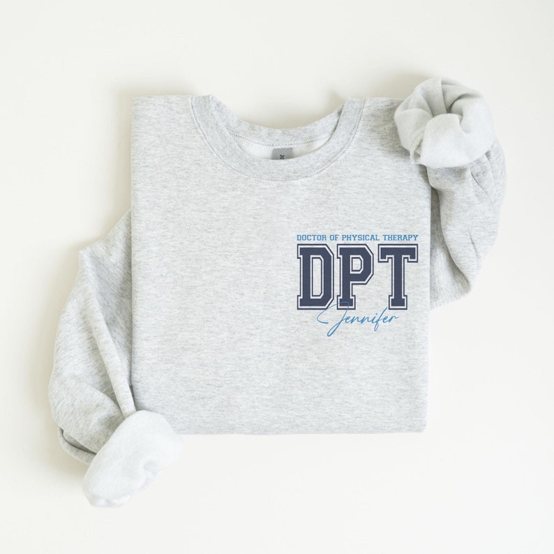 Puede incluir: Sudadera gris con el texto "Doctor of Physical Therapy DPT Jennifer" en letras azul marino y azul claro.
