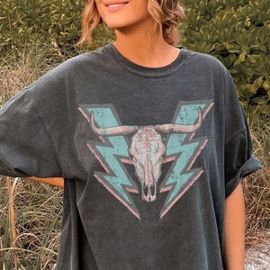 May include: A black oversized t-shirt with a graphic of a skull with horns and lightning bolts in pink and blue.
