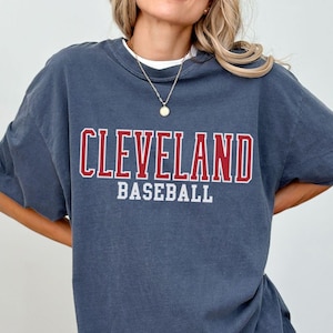 May include: A dark blue oversized t-shirt with the text "CLEVELAND BASEBALL" printed in red and white letters.