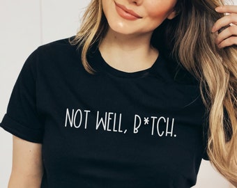 May include: Black t-shirt with the white text "NOT WELL, B*TCH." The shirt has short sleeves and a crew neck. The text is centered on the chest.