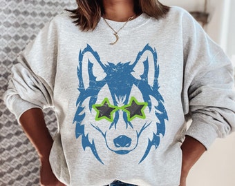 May include: A grey sweatshirt featuring a blue wolf graphic wearing green and black star-shaped sunglasses.