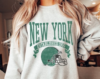 May include: Gray sweatshirt with a green graphic of a football helmet and the text "NEW YORK ESTABLISHED 1960".