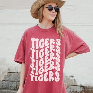 Peut inclure: Un t-shirt surdimensionn&eacute; rouge avec le mot "TIGERS" r&eacute;p&eacute;t&eacute; dans une police rose r&eacute;tro.