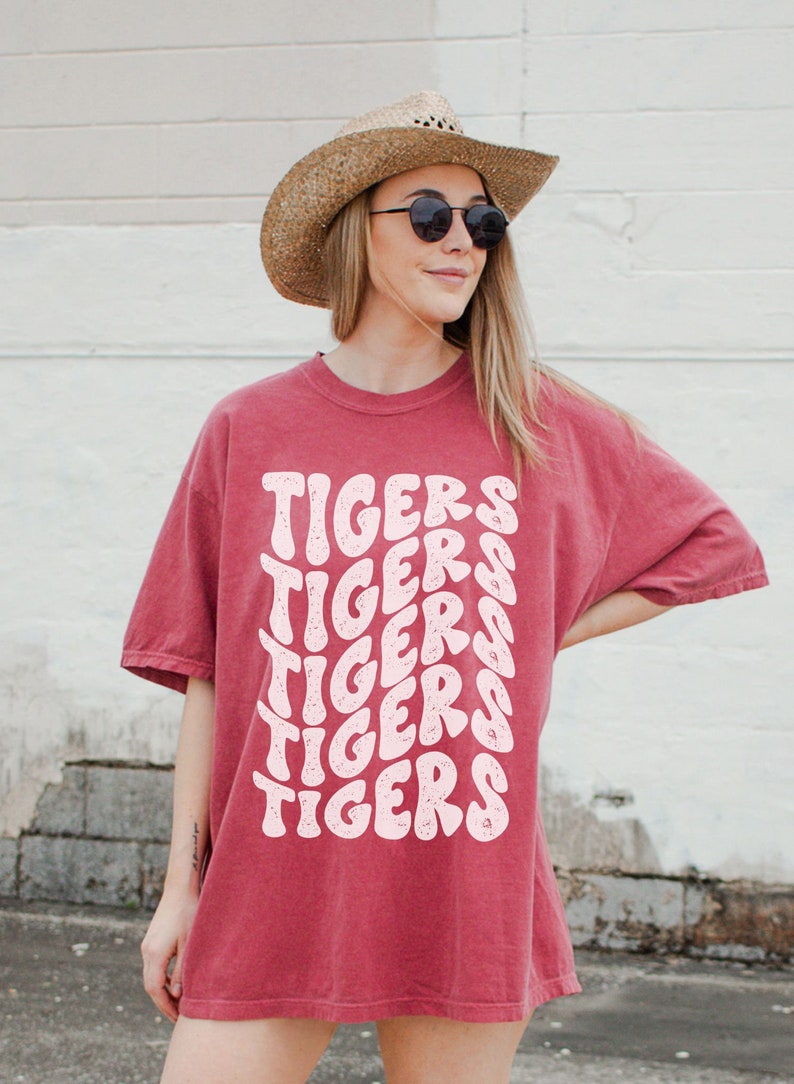 Peut inclure: Un t-shirt surdimensionn&eacute; rouge avec le mot "TIGERS" r&eacute;p&eacute;t&eacute; dans une police rose r&eacute;tro.