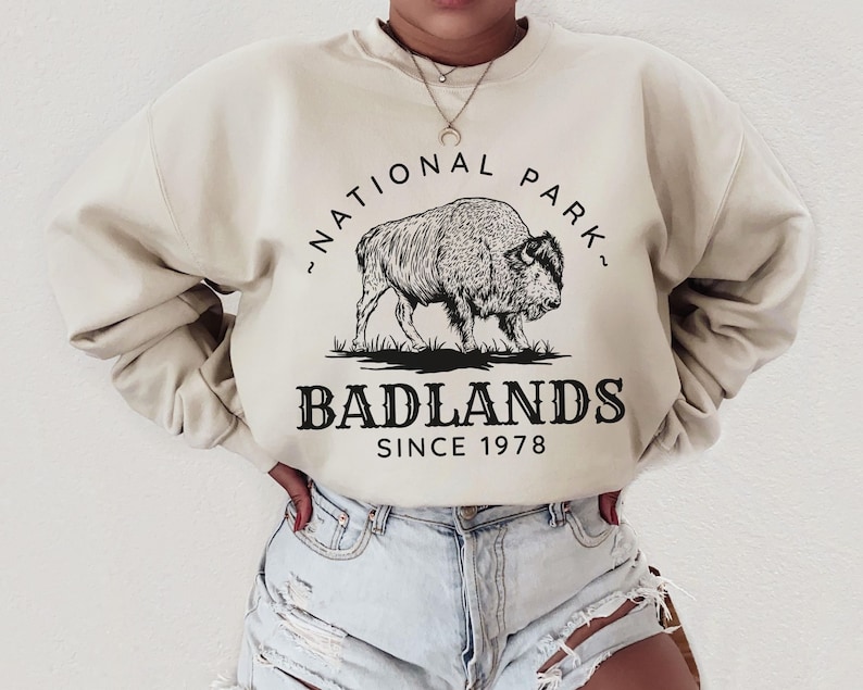 May include: A beige sweatshirt with a black graphic of a bison and the text "National Park, Badlands Since 1978".